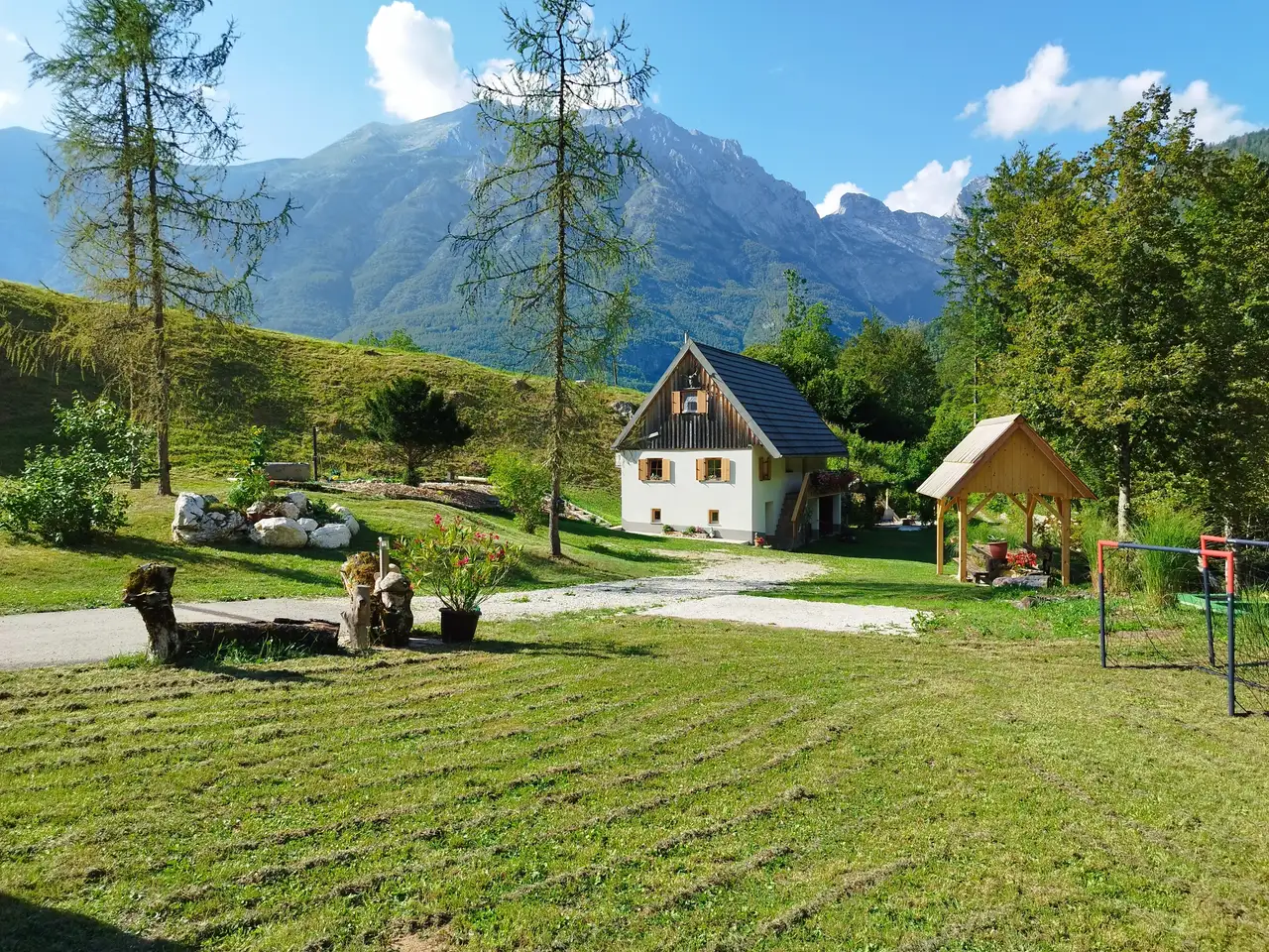 Hiša in senčnica na sončnem travniku pod gorami